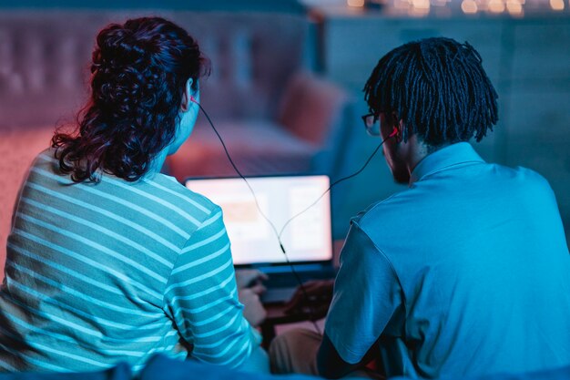 Vista posteriore delle coppie utilizzando laptop e auricolari a casa