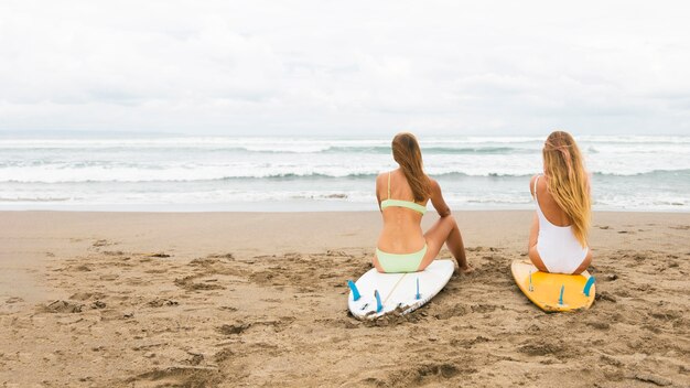 Vista posteriore di amiche in spiaggia con tavole da surf