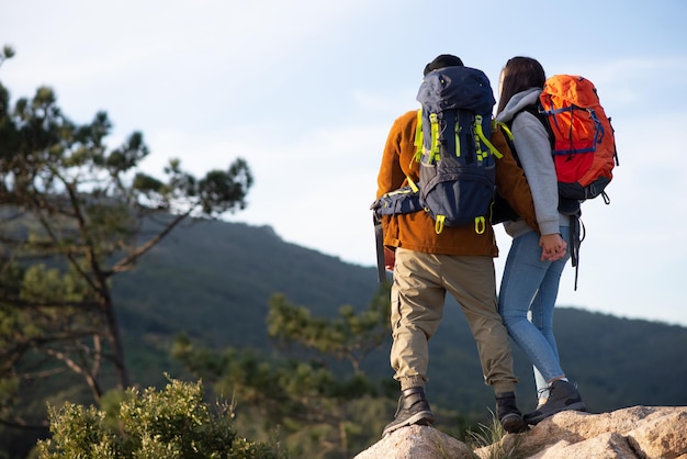 Vista posteriore di amici vivaci che fanno un'escursione. Uomo e donna in abiti casual con munizioni da trekking, tenendosi per mano. Natura, attività, concetto di hobby