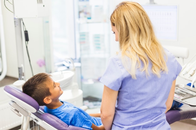 Vista posteriore di un dentista in piedi davanti al ragazzo seduto sulla poltrona del dentista