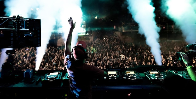 Vista posteriore di un DJ che suona musica davanti a una folla eccitata al festival musicale di notte