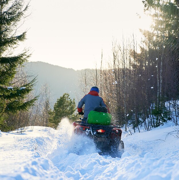 Vista posteriore di un motociclista che guida un fuoristrada a quattro ruote in inverno in montagna