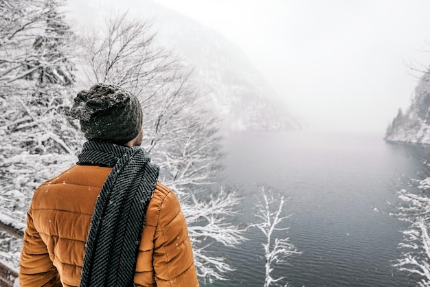 Vista posteriore di un uomo in abiti invernali che si gode l'inverno nebbioso vicino a un fiume di montagna