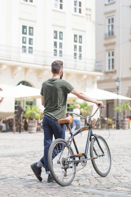 Vista posteriore di un uomo in piedi con la sua bicicletta sulla strada della città