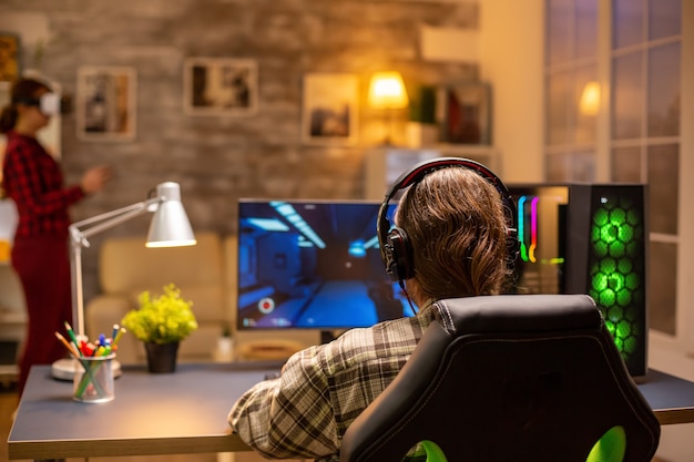 Vista posteriore di un videogiocatore professionista che gioca su un potente PC a tarda notte nel soggiorno.