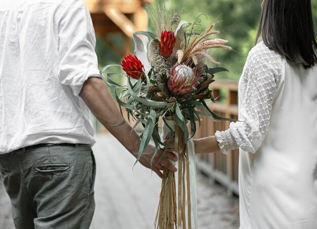 Vista posteriore di una coppia innamorata che tiene in mano un bouquet con fiori esotici di protea