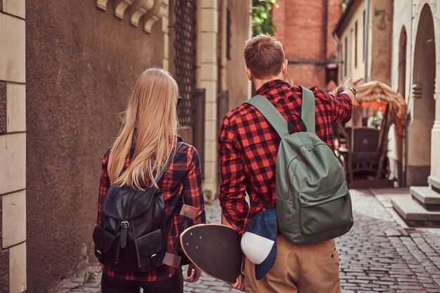 Vista posteriore di una giovane coppia hipster, bel pattinatore e la sua ragazza, tenendosi per mano, passeggiando per le vecchie strade strette d'Europa.