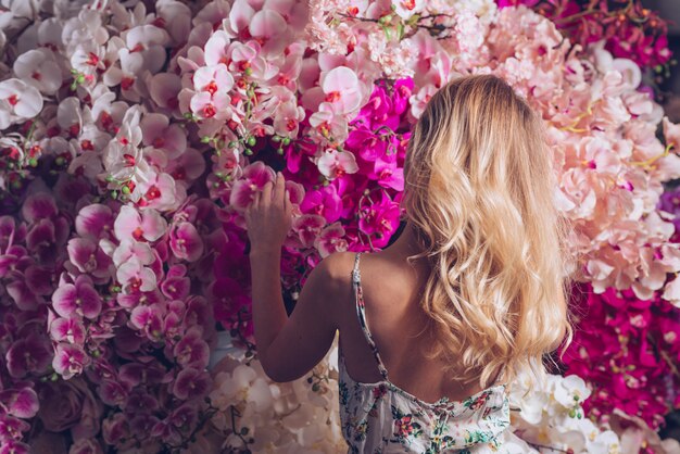 Vista posteriore di una giovane donna bionda guardando i fiori di orchidea