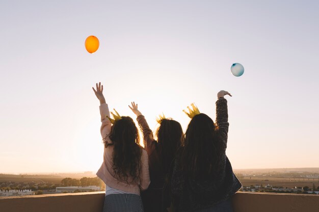 Vista posteriore ragazze che lanciano palloncini dal tetto