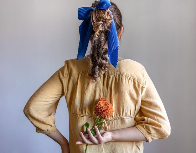Vista posteriore una ragazza tiene un fiore di crisantemo dietro la schiena sfondo grigio