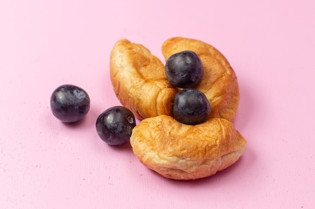 Vista ravvicinata anteriore deliziosi croissant al forno con ripieno di frutta insieme a prugnoli su sfondo rosa pasticceria cuocere