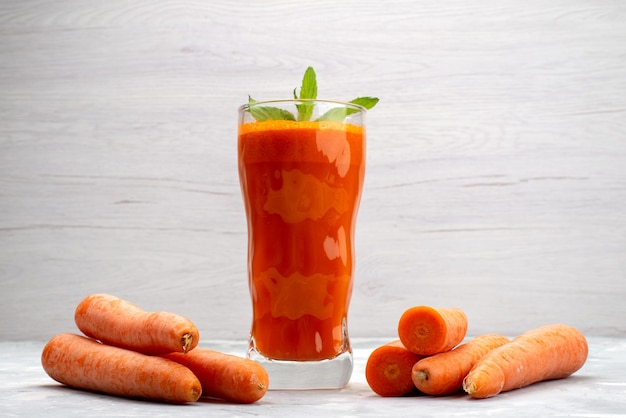 Vista ravvicinata anteriore succo di carota fresca all'interno di un bicchiere lungo con foglia e insieme a verdure di carote fresche