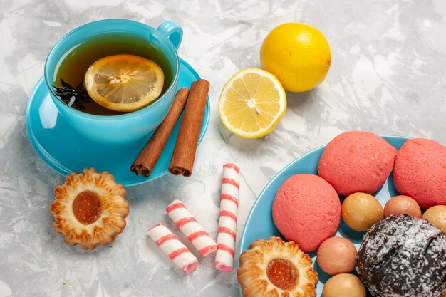 Vista ravvicinata anteriore tazza di tè con macarons francesi biscotti e torte sulla parete bianca luce zucchero biscotto torta dolce caramella biscotto