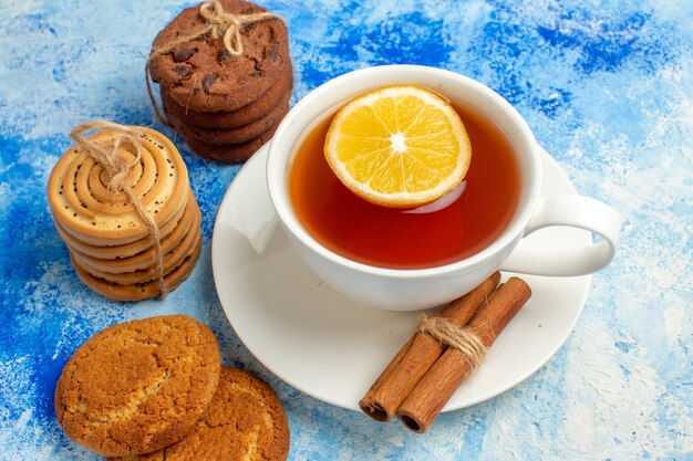 Vista ravvicinata dal basso tazza di tè aromatizzata con biscotti al limone e cannella legati con una corda sul tavolo blu
