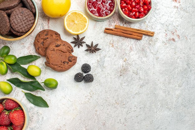 Vista ravvicinata dall'alto biscotti al cioccolato bastoncini di cannella biscotti al cioccolato ciotole di frutti di bosco agrumi sul tavolo