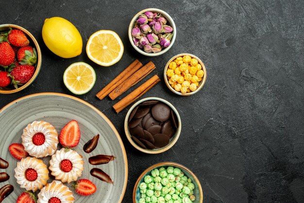 Vista ravvicinata dall'alto biscotti con cioccolato e fragole diversi dolci con tè nero limoni nocciole ciotole di cioccolato sul lato sinistro del tavolo