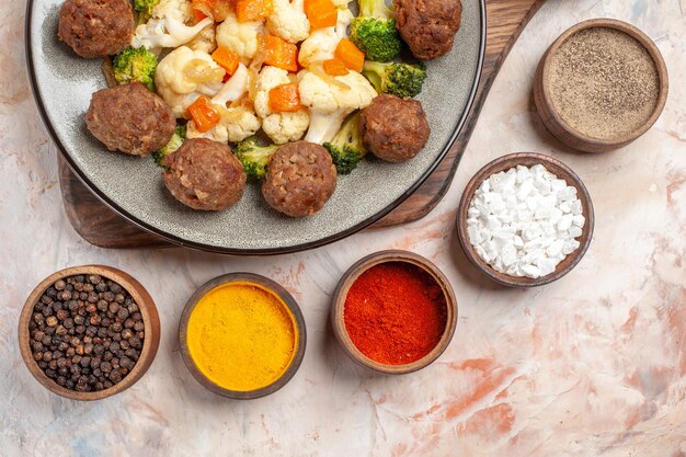 Vista ravvicinata dall'alto broccoli e cavolfiore insalata e polpetta sul piatto sul tagliere spezie diverse in piccole ciotole su sfondo nudo