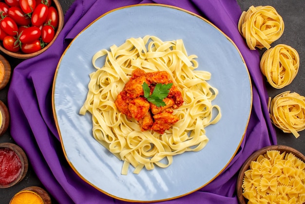 Vista ravvicinata dall'alto ciotole di pasta e salse di pomodori e diversi tipi di salse accanto al piatto di pasta e sugo sulla tovaglia viola