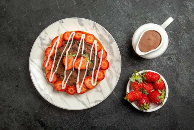 Vista ravvicinata dall'alto crema al cioccolato fragole ciotole di fragole e torta alla crema al cioccolato con fragole e cioccolato