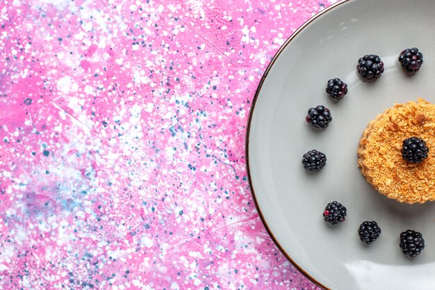 Vista ravvicinata dall'alto della piccola torta con frutti di bosco sulla superficie rosa