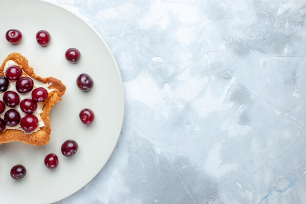 Vista ravvicinata dall'alto di amarene fresche all'interno della piastra con torta a forma di stella sulla scrivania a luce bianca, estate di vitamina di bacche acide di frutta