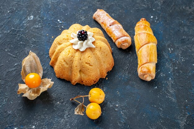 Vista ravvicinata dall'alto di una piccola torta deliziosa insieme a dolci banhles sulla scrivania scura