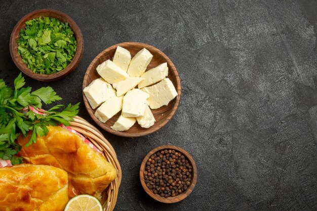 Vista ravvicinata dall'alto formaggio erbe ciotole di pepe nero erbe e formaggio e cesto di appetitose torte erbe limone e tovaglia a scacchi sul tavolo