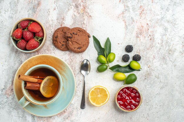 Vista ravvicinata dall'alto fragole fragole cioccolato biscotti agrumi melograno limone cucchiaio una tazza di tè con limone sul tavolo