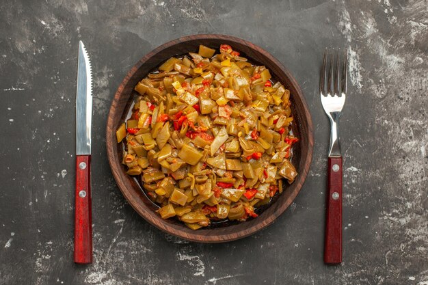 Vista ravvicinata dall'alto piatto appetitoso piatto appetitoso di fagiolini con pomodori tra forchetta e coltello sul tavolo scuro