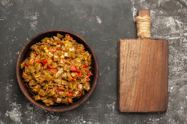 Vista ravvicinata dall'alto piatto appetitoso un piatto appetitoso di fagiolini e pomodori accanto al tagliere di legno sul tavolo scuro