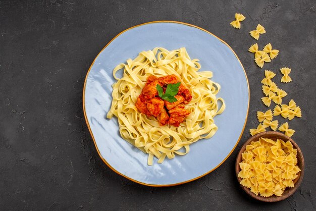 Vista ravvicinata dall'alto piatto di pasta piatto blu di pasta appetitosa con sugo e carne accanto alla ciotola di pasta sul tavolo scuro