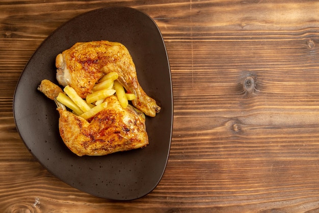 Vista ravvicinata dall'alto piatto fast food di patatine fritte e cosce di pollo sul lato sinistro del tavolo di legno