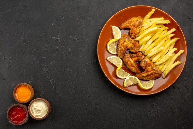 Vista ravvicinata dall'alto piatto fastfood di un appetitoso pollo con patatine fritte e limone a destra e tre tipi di salse sul lato sinistro del tavolo