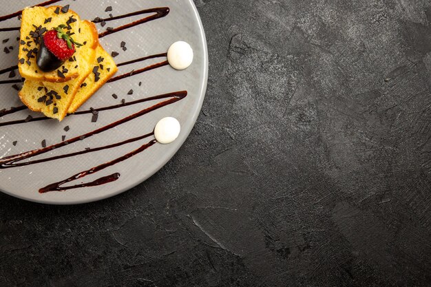 Vista ravvicinata dall'alto piatto grigio da dessert di torta appetitosa con fragole e salsa al cioccolato sul lato sinistro del tavolo scuro