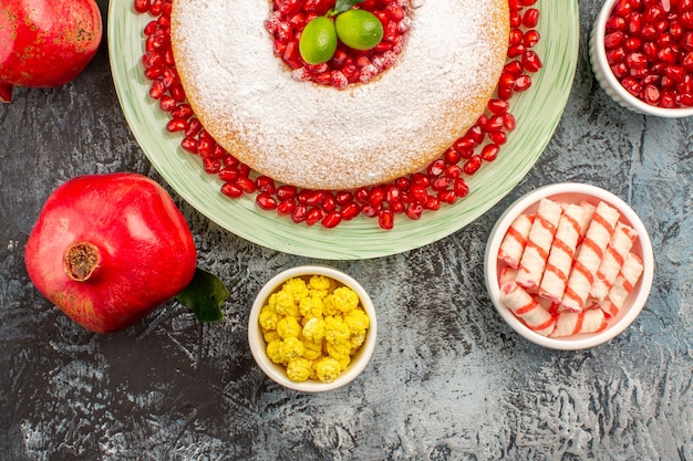 Vista ravvicinata dall'alto torta dolci una torta due melograni ciotole di caramelle colorate