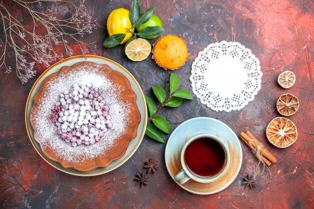 Vista ravvicinata dall'alto torta una torta con frutti di bosco agrumi cupcake pizzo centrino una tazza di tè