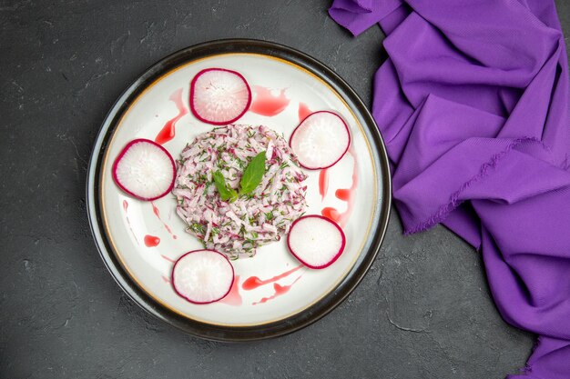 Vista ravvicinata dall'alto un piatto appetitoso di erbe di ravanello e tovaglia viola salsa