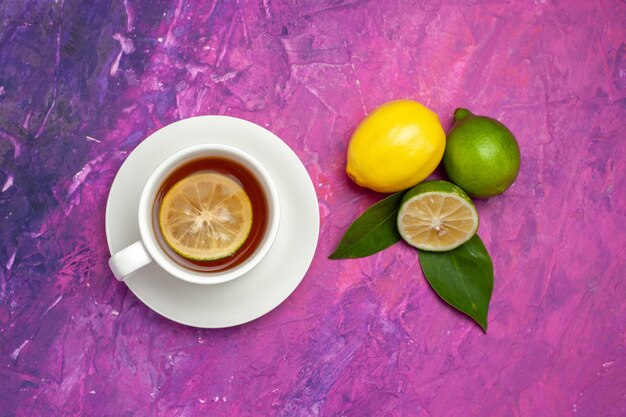 Vista ravvicinata dall'alto una tazza di tè lime e limone con foglie accanto alla tazza di gustoso tè al limone sul tavolo viola-rosa