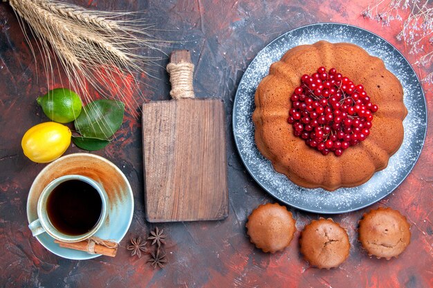 Vista ravvicinata dall'alto una tazza di tè una tazza di tè tavola di legno cupcakes torta con frutti di bosco limoni