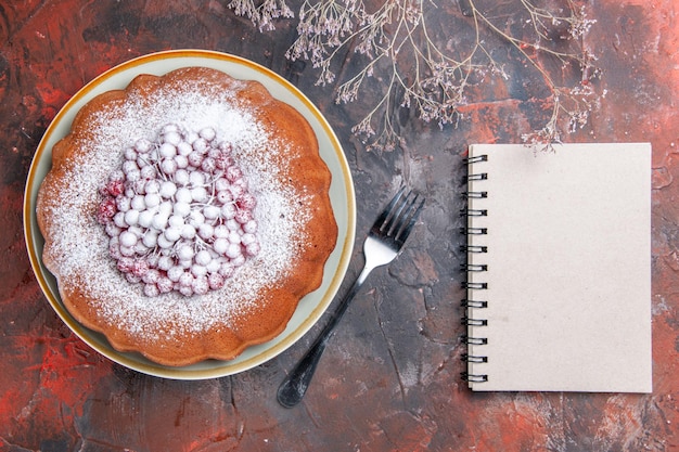 Vista ravvicinata dall'alto una torta un quaderno bianco con una forchetta accanto alla torta appetitosa con ribes rosso