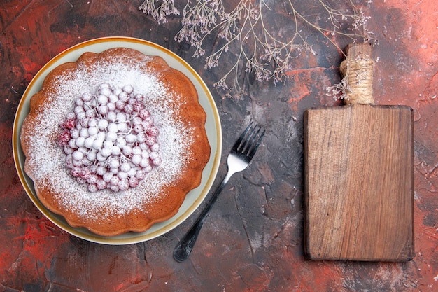 Vista ravvicinata dall'alto una torta una forchetta tagliere di legno accanto alla torta appetitosa con ribes rosso