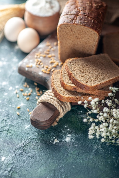 Vista ravvicinata dei frumenti del pane nero dietetico sul tagliere di legno farina di uova di fiori in una ciotola su sfondo blu