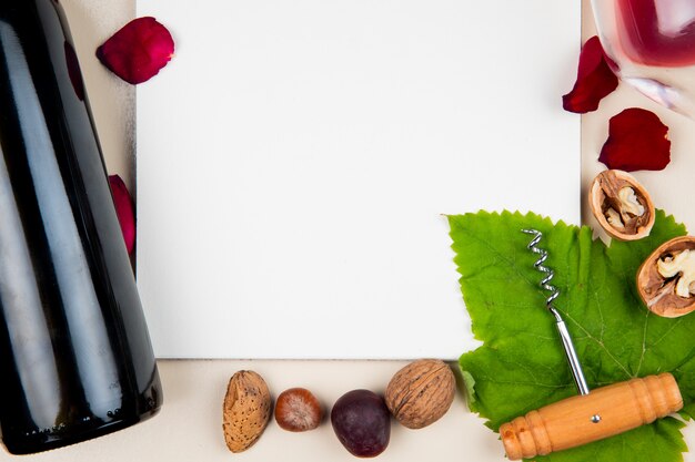 Vista ravvicinata del blocco note con bottiglia di vino rosso noci cavatappi e mandorle e petali di fiori intorno su bianco con spazio di copia