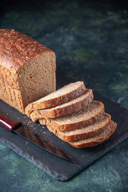 Vista ravvicinata del coltello per fette di pane nero su tavola di colore scuro su sfondo blu in difficoltà