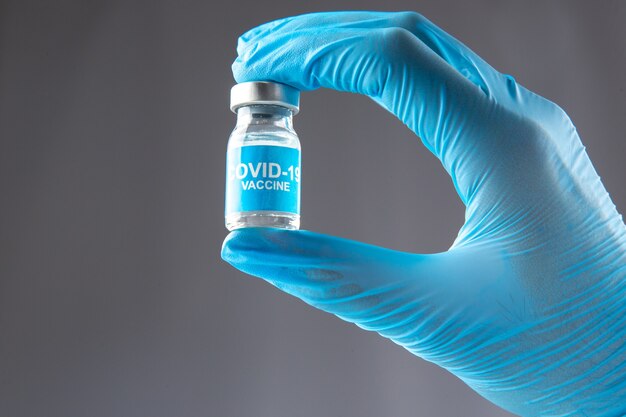 Vista ravvicinata del guanto blu che indossa la mano che tiene l'ampolla chiusa con vaccino contro il covid su sfondo grigio onda