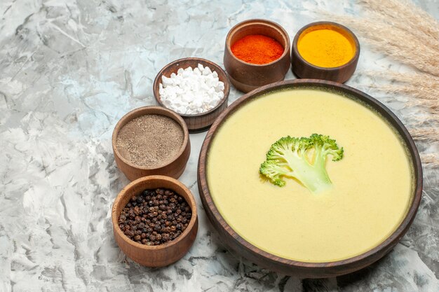 Vista ravvicinata della cremosa zuppa di broccoli in una ciotola marrone e diverse spezie sul tavolo grigio