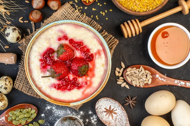 Vista ravvicinata della deliziosa colazione servita con marmellata di fragole in una ciotola e miele, cannella, lime, uova, cucchiai, su, colore scuro, fondo