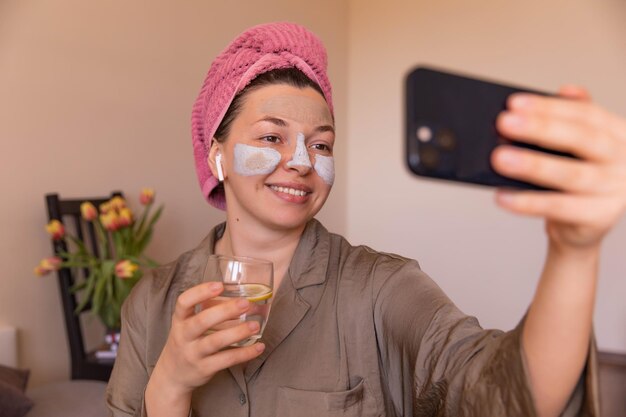 Vista ravvicinata della donna che parla di cura della pelle a casa facendo selfie con acqua di vetro