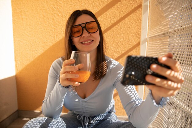 Vista ravvicinata della donna che sorride al telefono con occhiali da sole gialli sul balcone