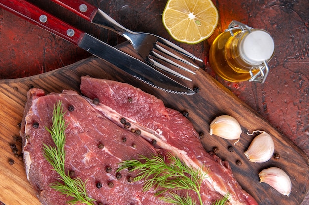 Vista ravvicinata di carne rossa su tagliere di legno e bottiglia di olio di pepe verde all'aglio per e coltello su sfondo scuro immagine stock